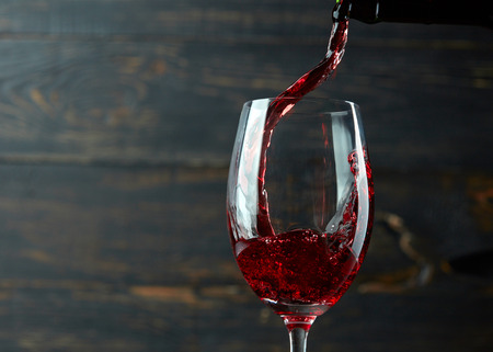 47409628 - pouring red wine into the glass against dark wooden background